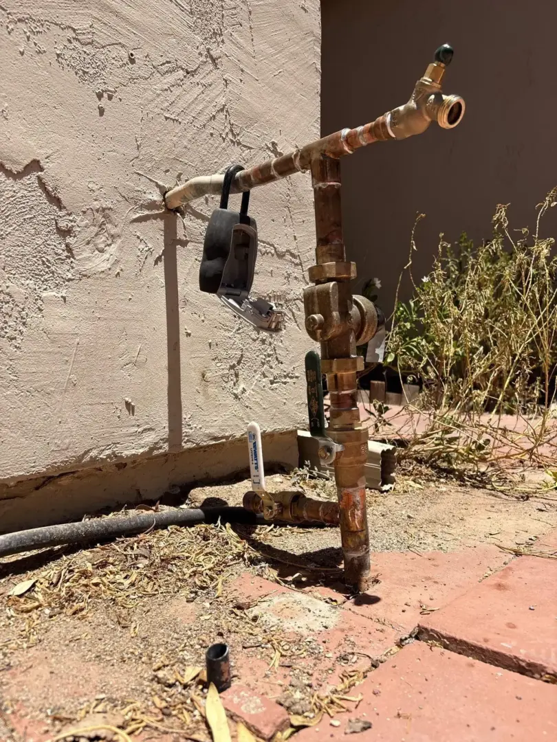 Main Water - Angela - Blacktail Restoration Outdoor irrigation valve and piping with rusted fittings, set against a stucco wall; a black plastic device hangs from the pipe.